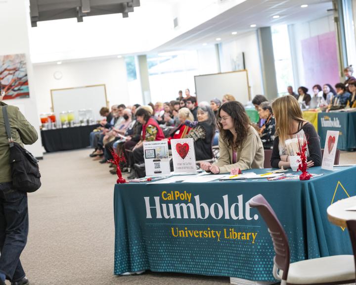 Photos depicts audience in rows of chairs, welcome table, catering in the background