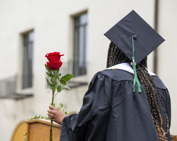 Photo of Umoja Alumni facing the audience in grad regalia, holding a rose for the "Rose Ceremony"
